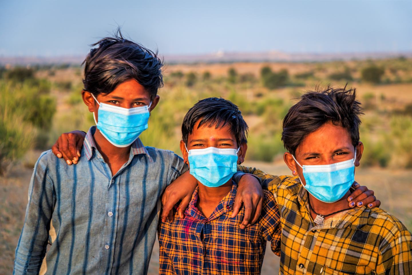 Young Indian boys wearing medical masks pose in the Thar Desert. Sustainability innovation green agriculture.